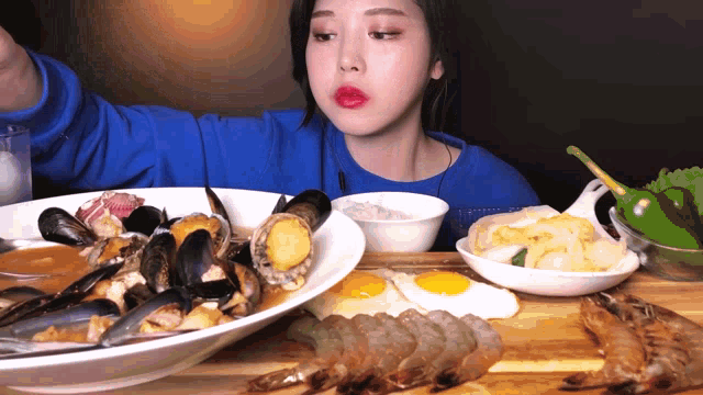 a woman in a blue sweater is eating a large plate of food