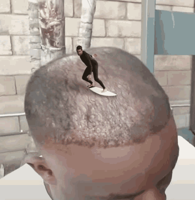 a man in a wetsuit is riding a surfboard on top of a man 's head