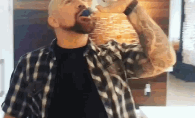 a man in a plaid shirt is drinking from a bottle .