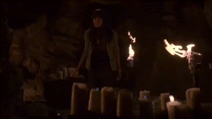a woman stands in front of a row of lit candles in a dark room