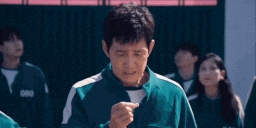 a man in a green jacket is pointing at something in front of a group of children .