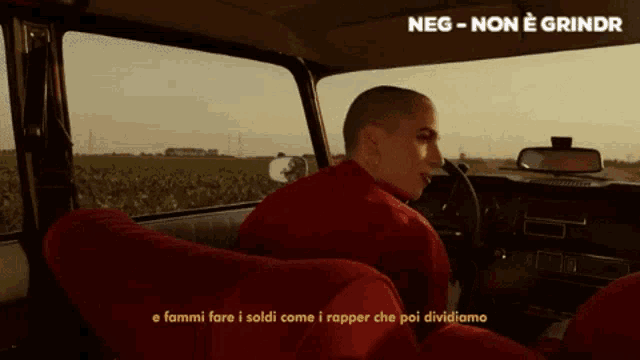a man in a red shirt is sitting in a car with the words neg-non e grindr written above him