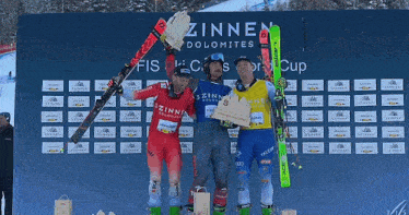 three skiers are standing on a podium in front of a sign that says zinnen dolomites