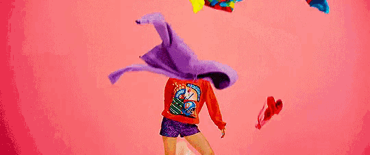 a woman in a red sweater and shorts is standing in front of a pile of clothes .