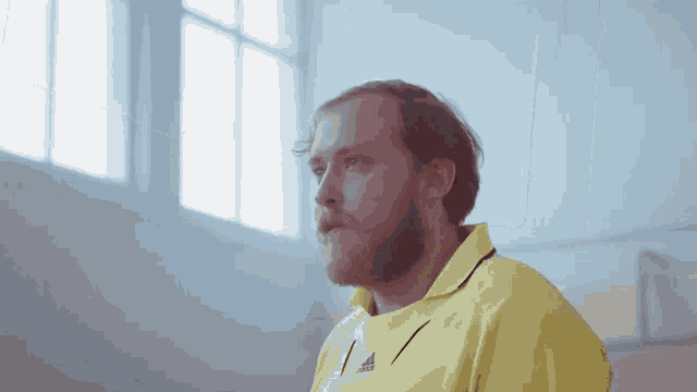 a man wearing a yellow adidas shirt looks to his left