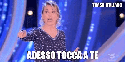 a woman in a polka dot dress says " adesso tocca a te " on a blue background