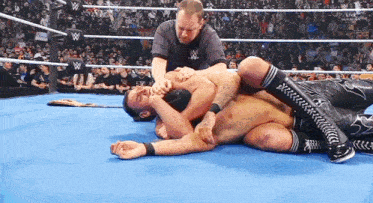a man is laying on the ground in a wrestling ring while a referee watches .