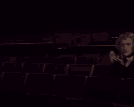 a man in a wig is sitting in an empty auditorium clapping .