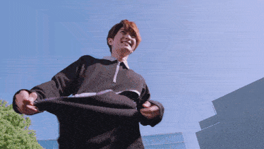 a man in a black sweater is standing in front of a building with a blue sky in the background
