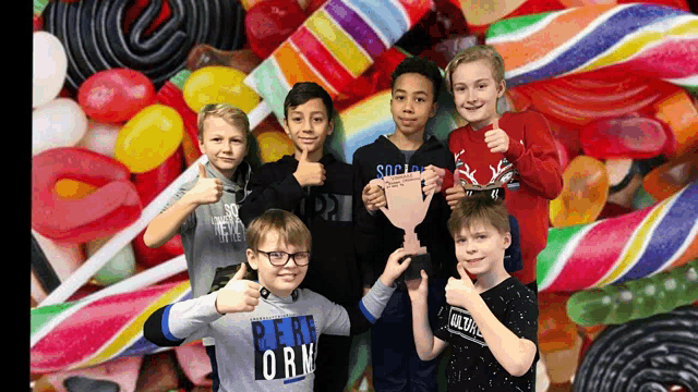 a group of young boys are giving a thumbs up in front of a wall of candy