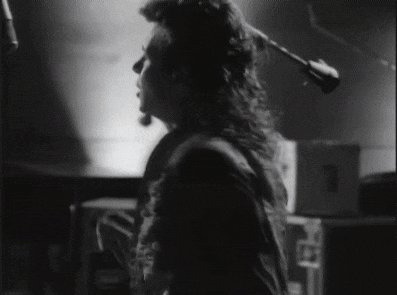 a black and white photo of a person playing a guitar in front of a microphone .