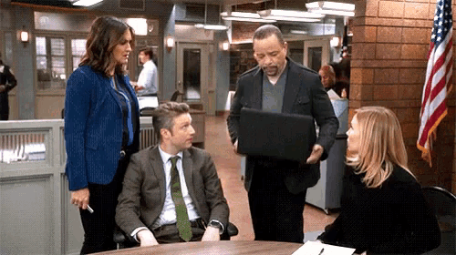 a group of people are gathered around a table including a man in a suit holding a laptop