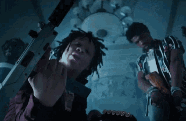 a man with dreadlocks is holding a gun in a dark room while another man holds a gun .