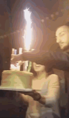 a man and a woman holding a cake with a firework going off in the background
