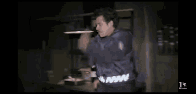 a man is smoking a cigarette in a dark room while wearing a blue jacket .