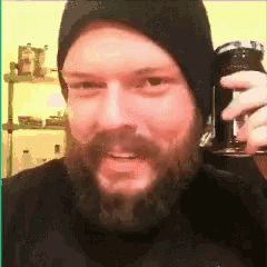 a man with a beard wearing a black hat holds a can of soda