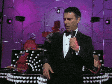 a man in a tuxedo is holding a microphone in front of a purple background