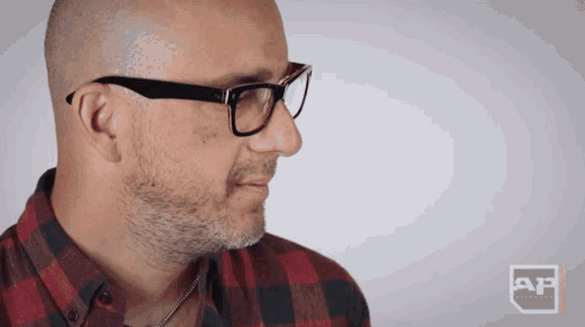 a man wearing glasses and a plaid shirt with ap written on the bottom