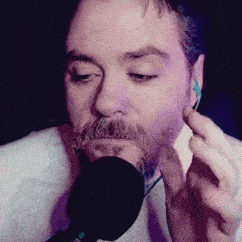 a man with a beard and ear buds is singing into a microphone