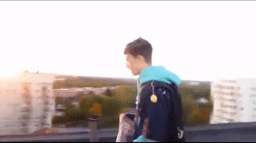 a man in a blue jacket with the letter s on the back walks on a rooftop