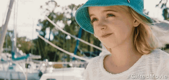 a little girl wearing a blue hat and a white shirt is standing in front of boats ..
