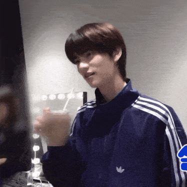 a young man wearing a blue adidas jacket is drinking from a glass with a straw