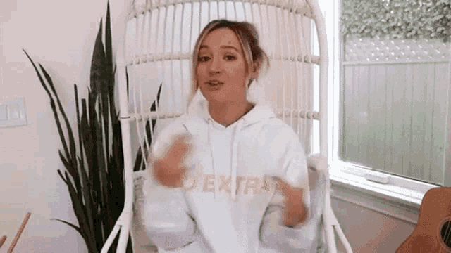 a woman in a white hoodie is sitting in a chair in front of a window .