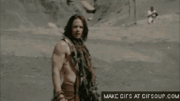 a man without a shirt is standing in the desert holding a skull in his hand .