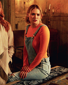 a woman wearing overalls sits on a table