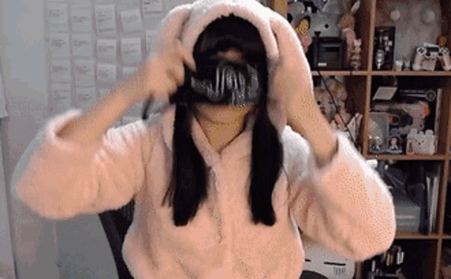 a woman wearing a bunny ear hoodie is covering her mouth with a mask .