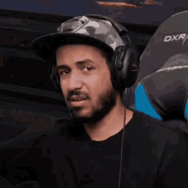 a man with a beard wearing headphones and a hat is sitting in a gaming chair .