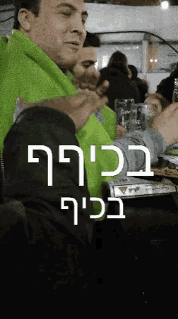 a man in a green jacket is sitting at a table with a glass of beer