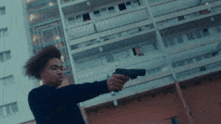 a man with curly hair is pointing a gun at a building