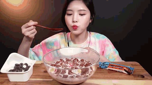 a woman is eating a bowl of cereal with a spoon and a chocolate bar next to her