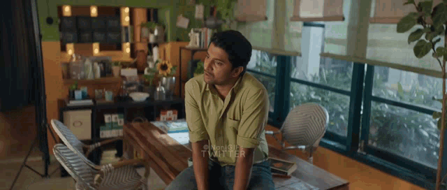 a man in a green shirt sits in front of a window with twitter written on the bottom right