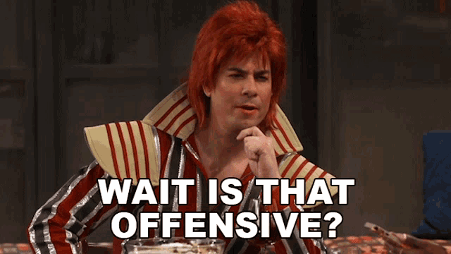 a man with red hair is sitting at a table with the words wait is that offensive below him