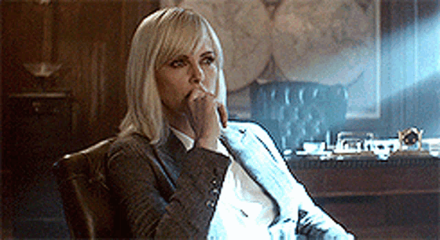 a woman in a suit and tie is sitting in a chair with her hand on her chin .