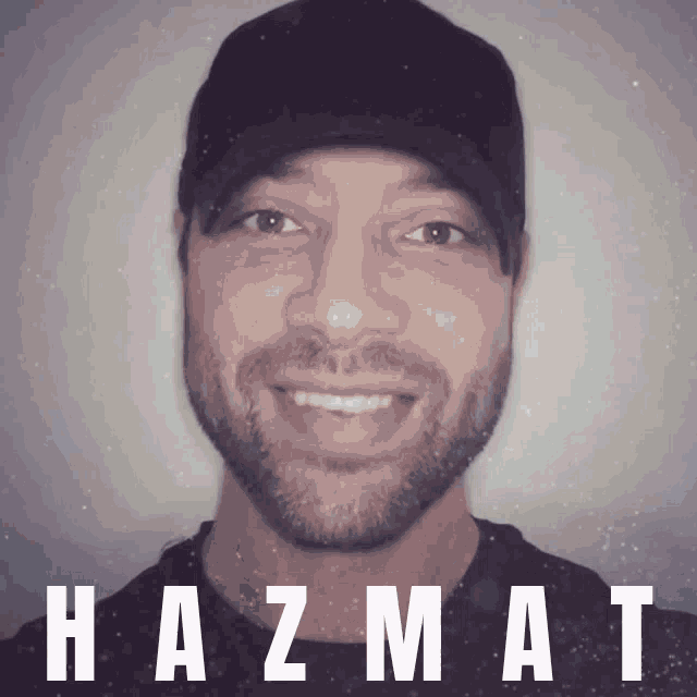 a man with a beard wearing a black hat with hazmat in white letters behind him