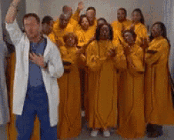 a man in a white coat stands in front of a group of people wearing yellow robes