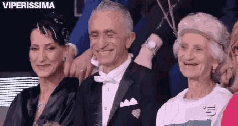 a man in a tuxedo and bow tie is sitting next to two women .