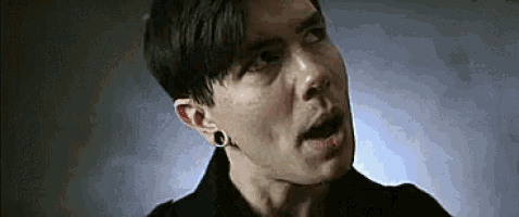 a close up of a man wearing a black shirt and earrings making a funny face .