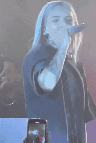 a woman singing into a microphone with the letter e on her shirt visible