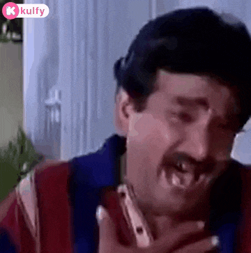 a man with a mustache is talking on a cell phone and making a funny face .