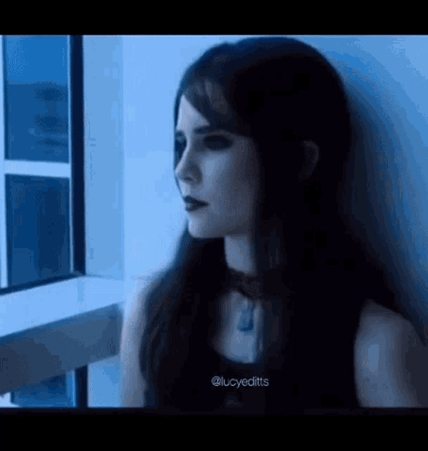 a woman in a black dress is leaning against a wall looking out a window .