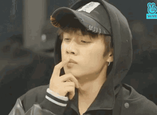 a close up of a person wearing a hat and a hoodie with their hand on their chin .