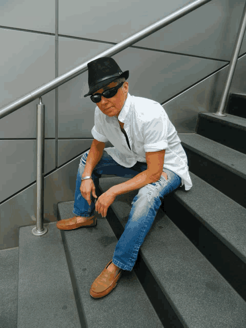 a man wearing a hat and sunglasses sits on the stairs