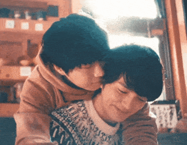 two young men are hugging each other in a room . one of the men is wearing a sweater .