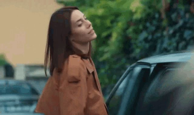 a woman in a brown coat is standing in front of a car .