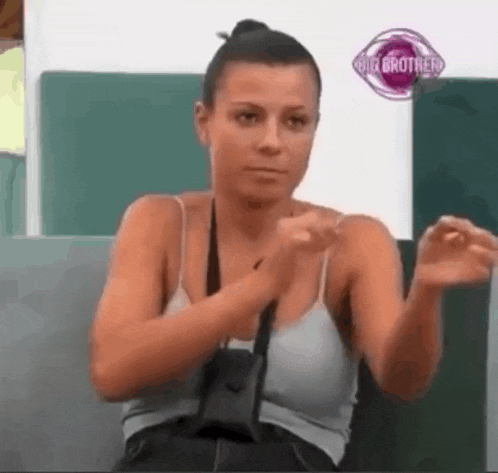 a woman in a tank top is sitting on a couch with her hands up .