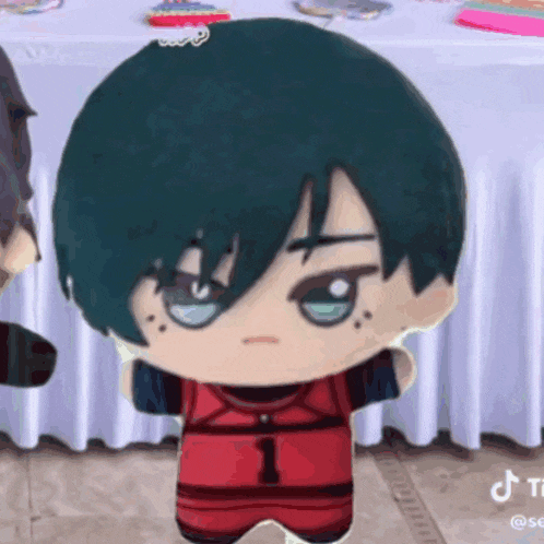 a stuffed doll with green hair and blue eyes is standing in front of a white table cloth .